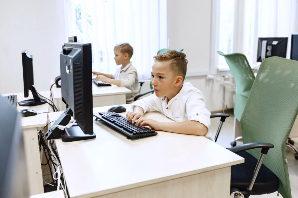 Two young boys focused on computers in a bright, modern classroom setting.