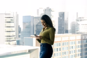 A businesswoman stands at a glass office window overlooking a city, representing corporate ambition
