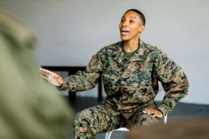 A woman in military uniform speaks at a podium with flags in the background