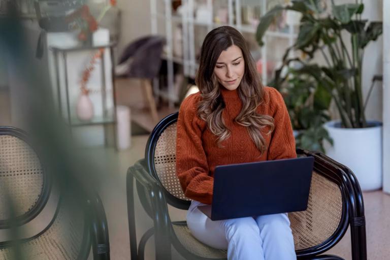 A woman entrepreneur reviewing work on a laptop at a bright office desk