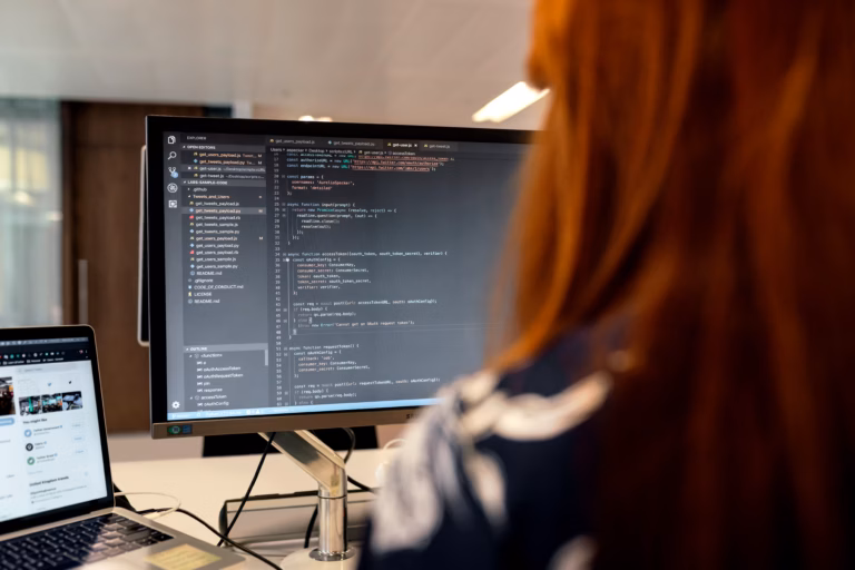 A woman focused on her laptop, surrounded by code on multiple screens, illustrating technical work