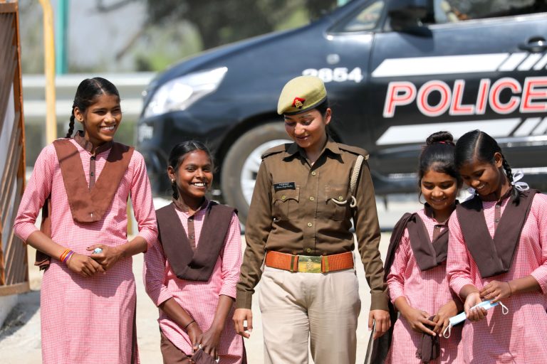 A uniformed police officer standing with schoolgirls beside a police vehicle