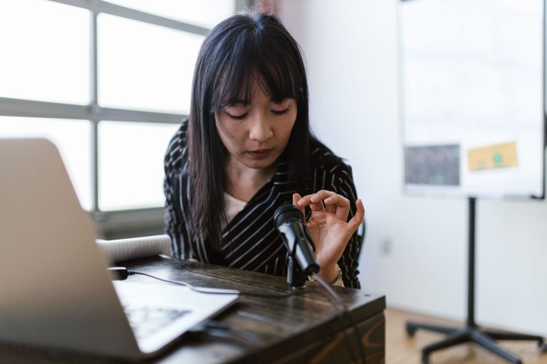 Female Founder Challenges Robotics' PhD Assumption with $280M Startup 2 A woman in an office setting testing a microphone while sitting at a desk with a laptop