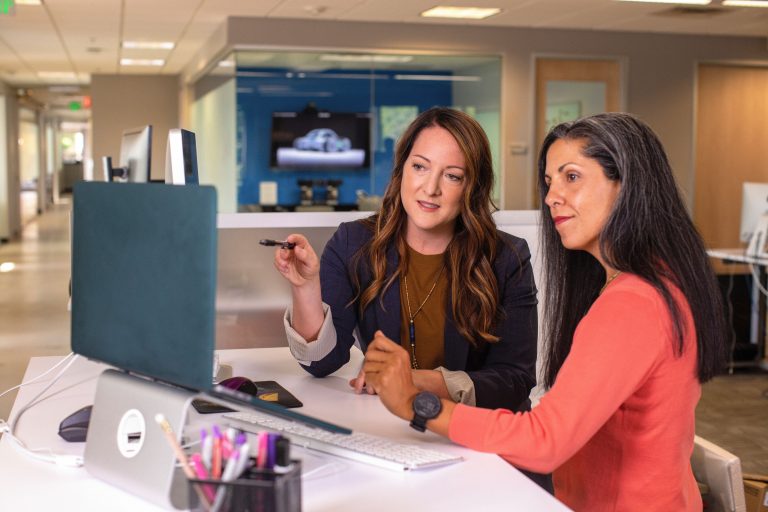 How Managers Can Support Women Through Motherhood and Career Transitions 1 Two professional women discussing project details together in a modern office environment