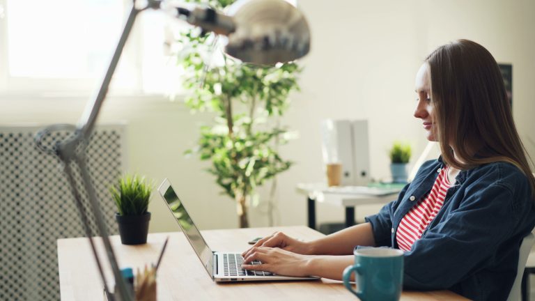 Woman smiling while working on a laptop in a modern office with plants