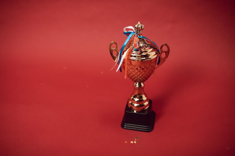 A gold trophy with colored ribbons against a red background