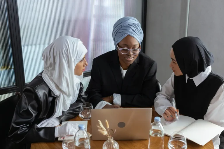 Three Muslim businesswomen in hijabs working together on a laptop in an office setting