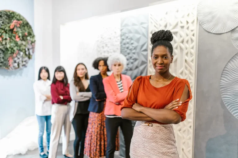 A confident female leader stands with diverse female colleagues in a modern office setting