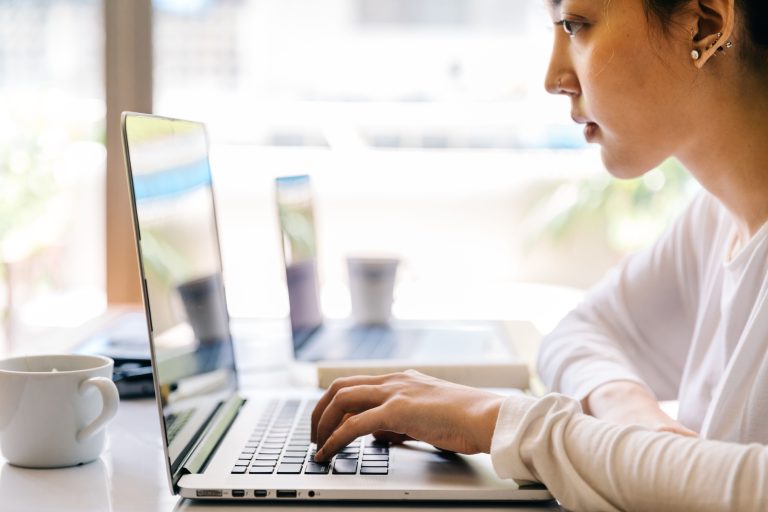 Laid-Off Workers Back: 39% Of Women Would Return, Survey Finds 2 Woman typing on a laptop beside a window