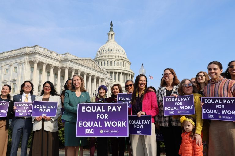 DWC Members Unveil Bills On Childcare, Pay And Business 2 Democratic Women’s Caucus members holding equal-pay signs outside the Capitol