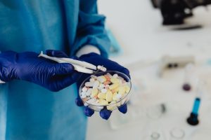 Gloved hands use tweezers to examine tablets in a petri dish