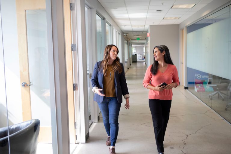 Two women walking and talking in an office corridor